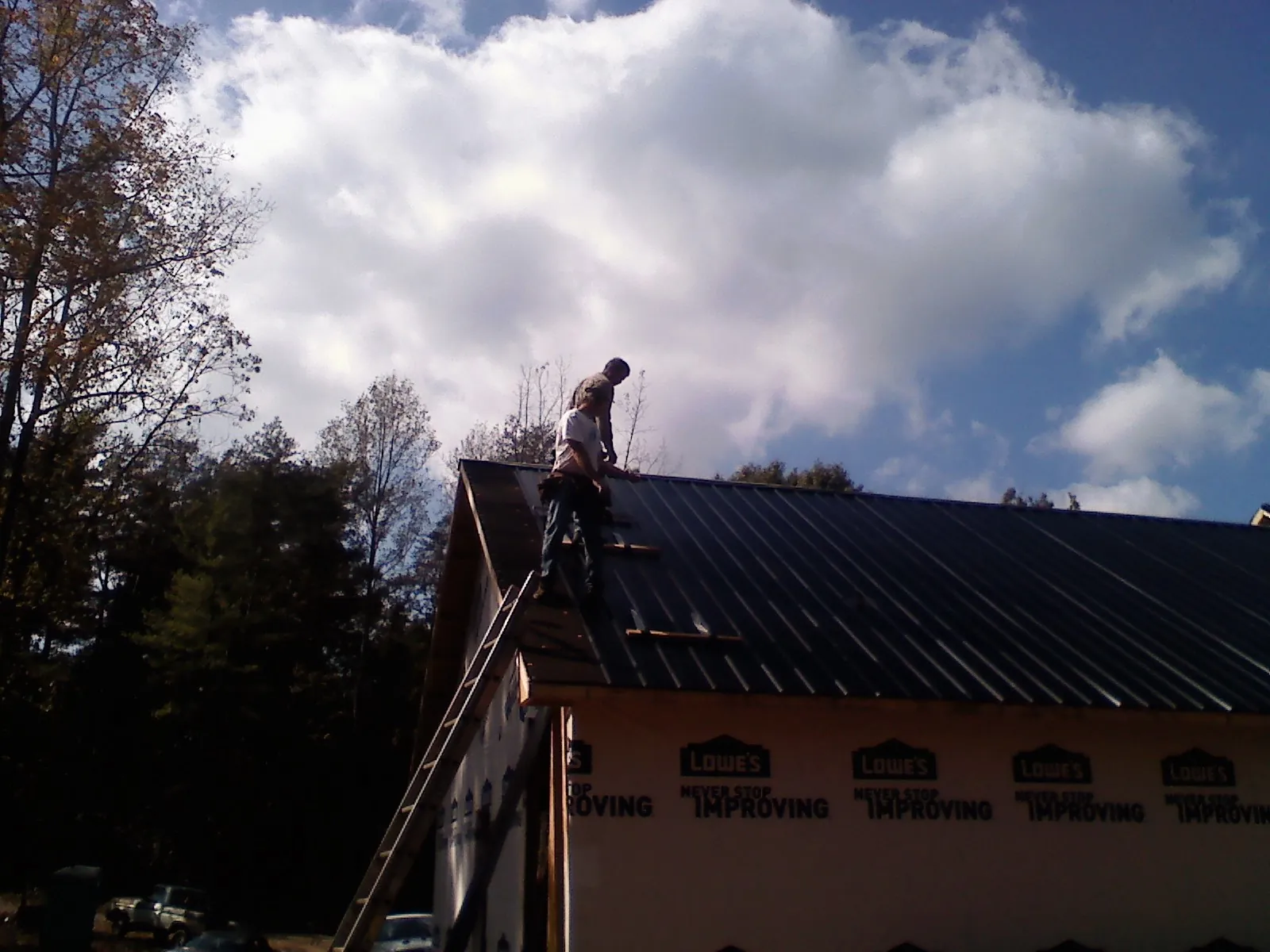Roofer fastening dark metal panels high against a cloudy sky in Buffalo